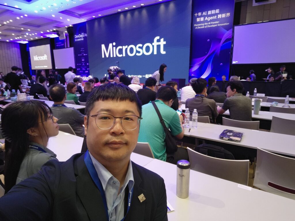 我坐在會場座位上自拍,背景是 Microsoft 的大型舞台螢幕
